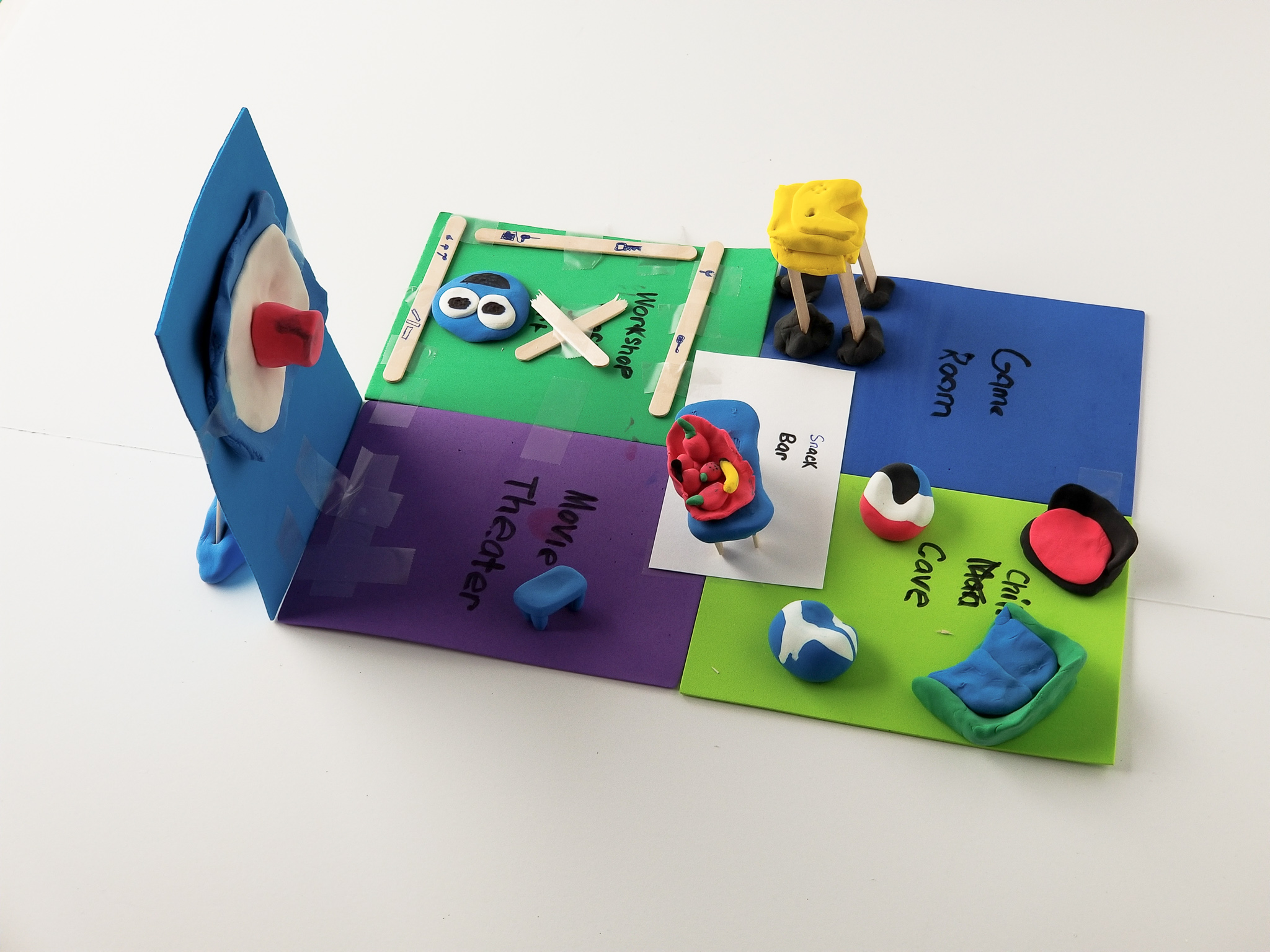 A hand-built model from the workshop: a foam-board floor plan of "The Ultimate Hangout" with a game room, movie theater, snack bar, and chill-out cave modelled in clay.